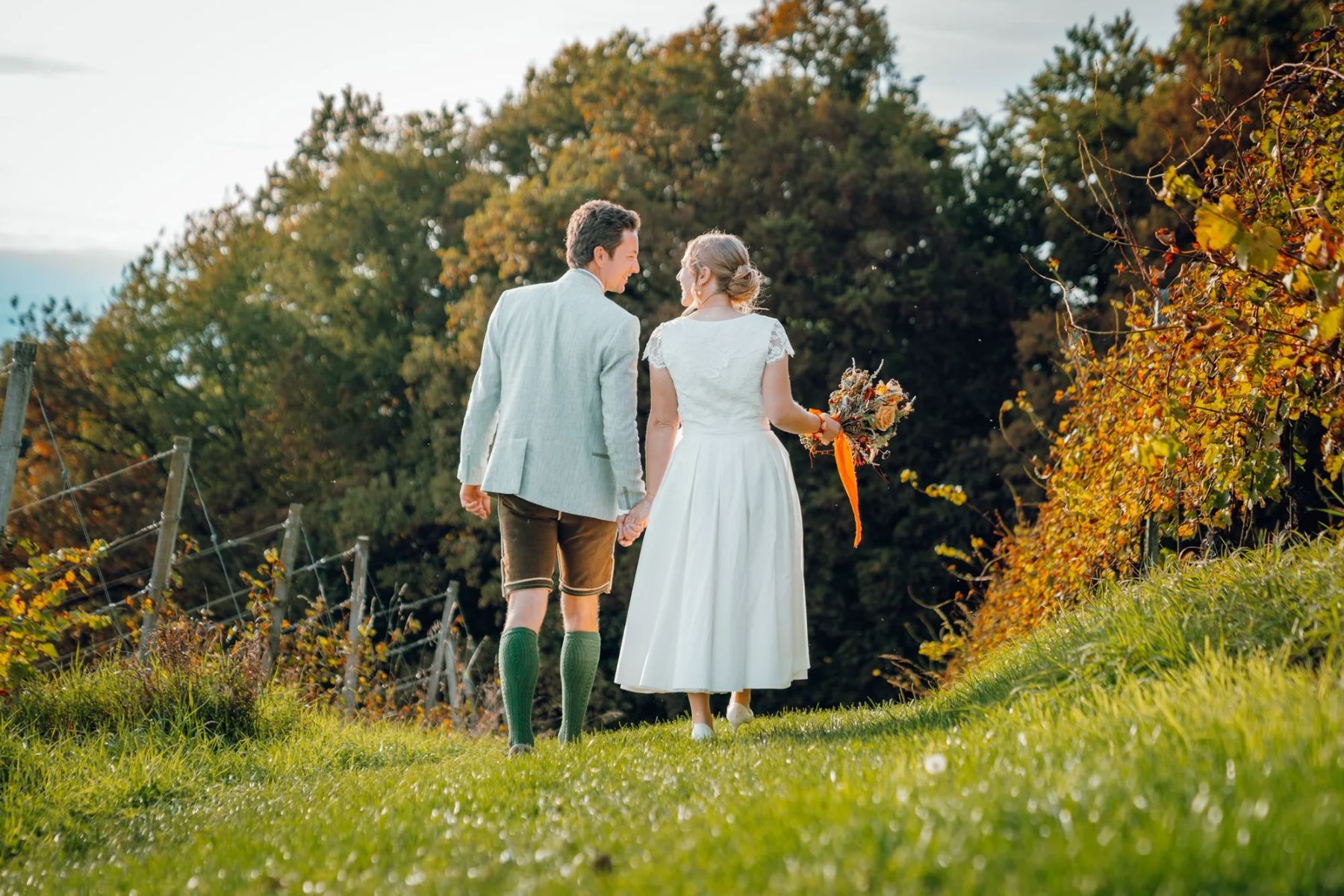 Brautpaar geht Hand in Hand durch eine herbstliche Wiese